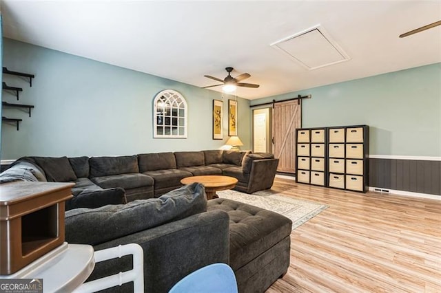 living room with a barn door, ceiling fan, wood finished floors, and wainscoting