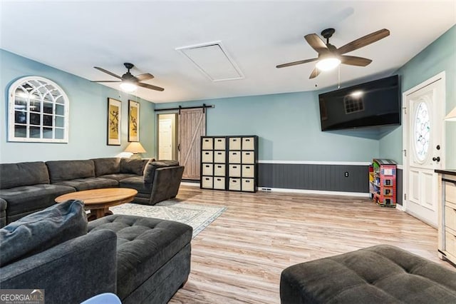 living area featuring ceiling fan, a barn door, a wainscoted wall, and wood finished floors