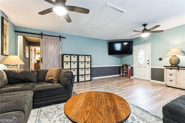 living room featuring a wainscoted wall, a barn door, wood finished floors, and a ceiling fan