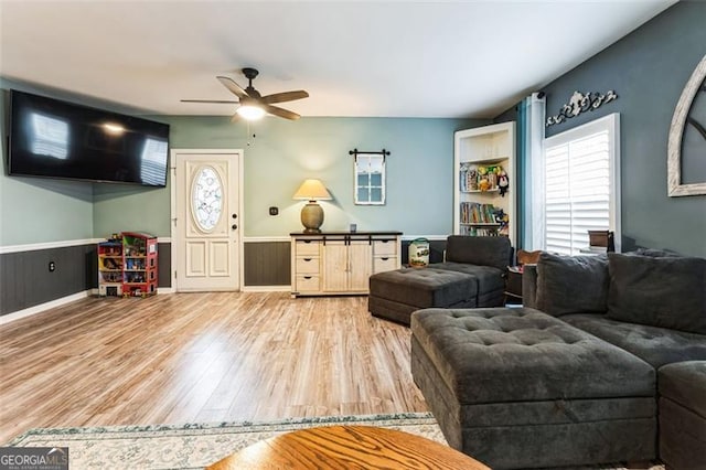 living area with wainscoting, light wood-style flooring, and a ceiling fan