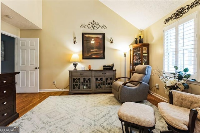 sitting room with lofted ceiling, a textured ceiling, wood finished floors, and baseboards