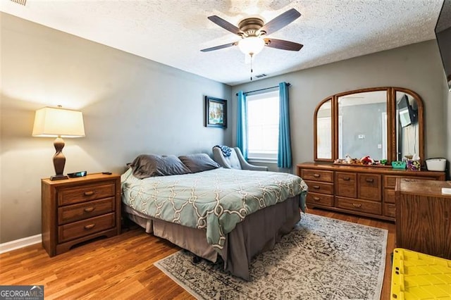 bedroom with a textured ceiling, ceiling fan, wood finished floors, and visible vents