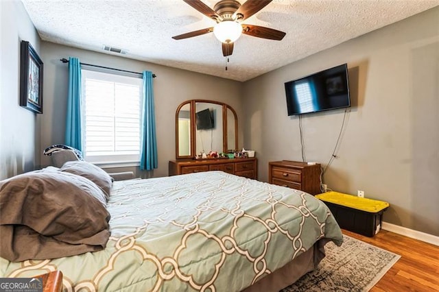 bedroom featuring a textured ceiling, wood finished floors, visible vents, and baseboards