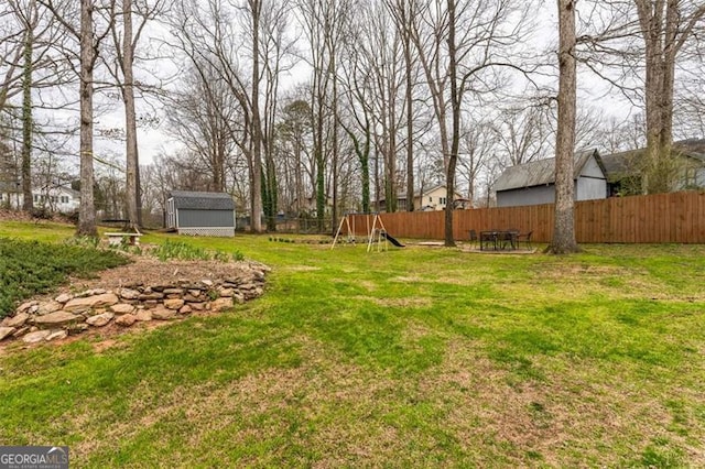 view of yard with a fenced backyard, a storage unit, a playground, and an outdoor structure