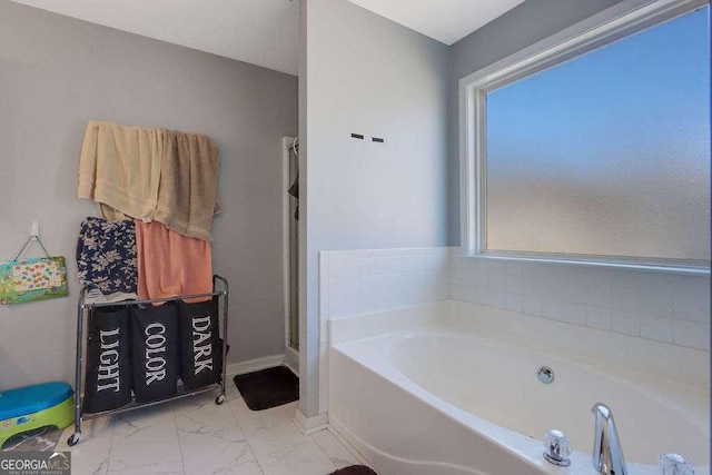 bathroom featuring marble finish floor, baseboards, and a bath