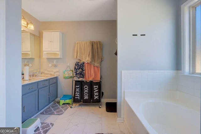 full bathroom with marble finish floor, baseboards, a garden tub, and vanity