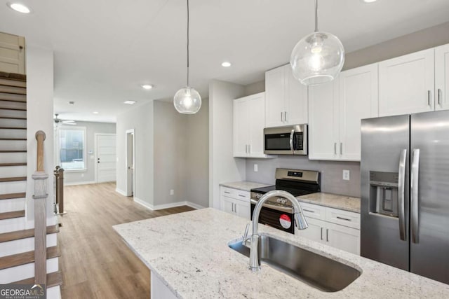 kitchen featuring a sink, white cabinets, light wood-style floors, hanging light fixtures, and appliances with stainless steel finishes