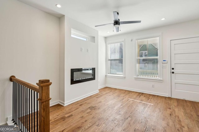 entrance foyer featuring a glass covered fireplace, baseboards, light wood finished floors, and recessed lighting