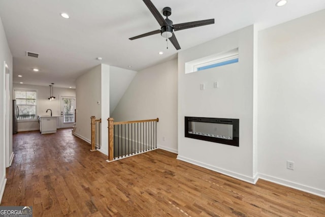 unfurnished living room with a glass covered fireplace, wood finished floors, visible vents, and recessed lighting