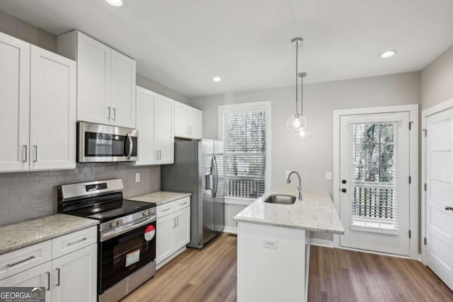 kitchen with stainless steel appliances, a sink, light wood-style flooring, and decorative backsplash