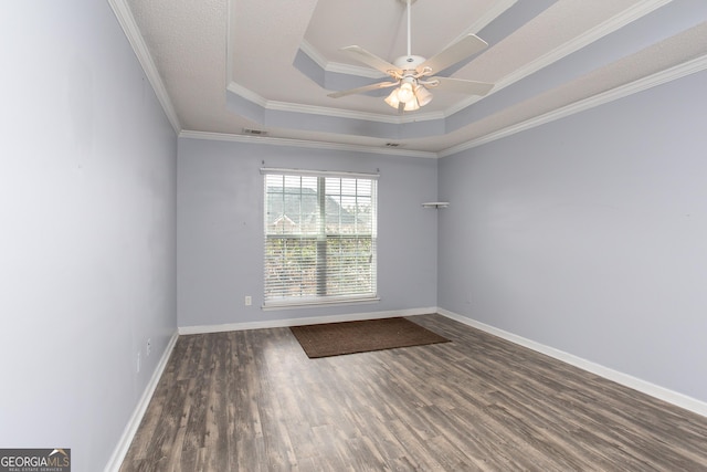 empty room featuring a tray ceiling, visible vents, baseboards, and wood finished floors