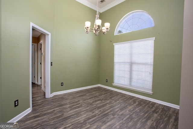 empty room with a chandelier, dark wood-type flooring, a high ceiling, baseboards, and crown molding