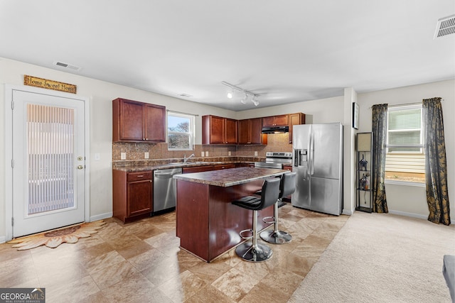 kitchen featuring visible vents, a kitchen breakfast bar, dark countertops, stainless steel appliances, and decorative backsplash