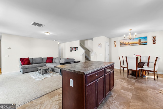 kitchen featuring visible vents, a kitchen island, dark countertops, a notable chandelier, and light colored carpet