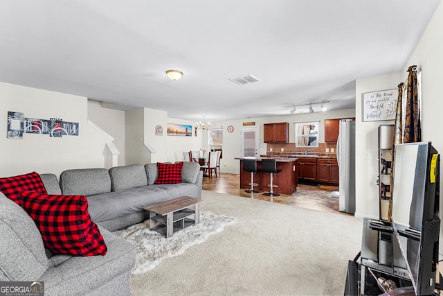 living room featuring visible vents, light colored carpet, track lighting, and a notable chandelier