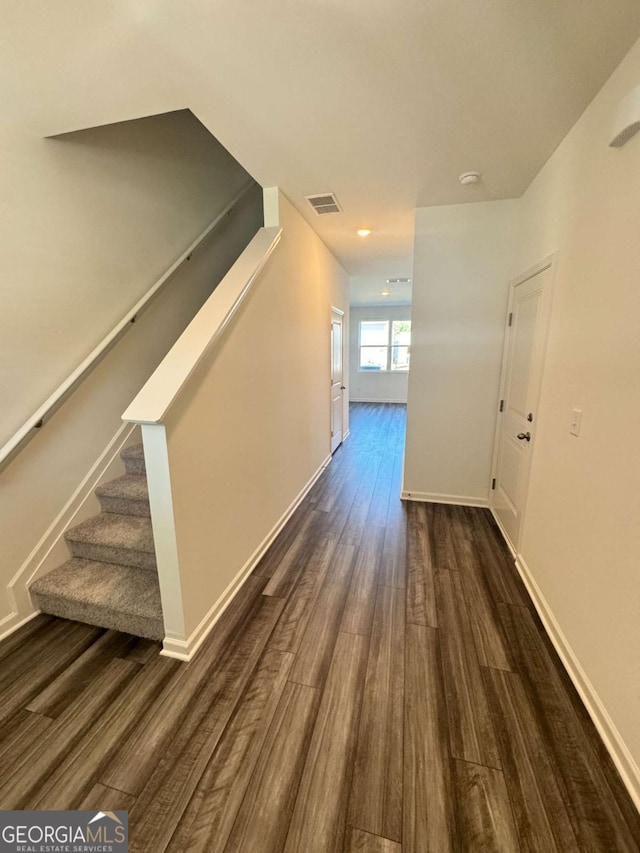 corridor with dark wood-style floors, baseboards, stairs, and visible vents