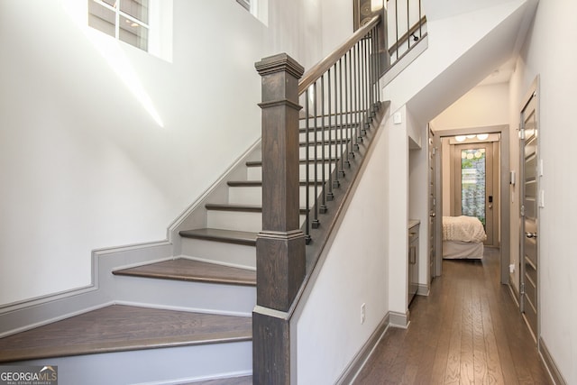 staircase featuring a towering ceiling, hardwood / wood-style flooring, and baseboards