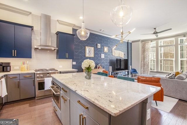 kitchen featuring stainless steel appliances, wood finished floors, a kitchen island, open floor plan, and wall chimney exhaust hood