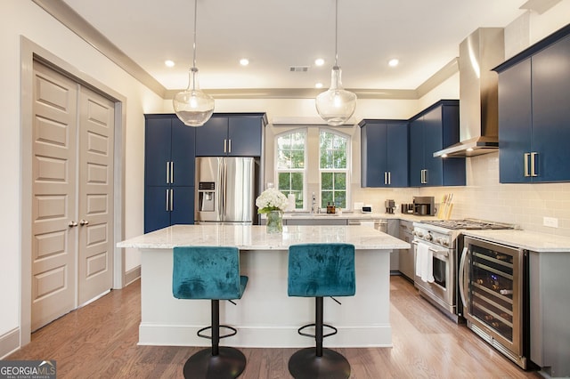 kitchen featuring blue cabinetry, appliances with stainless steel finishes, wine cooler, and wall chimney range hood