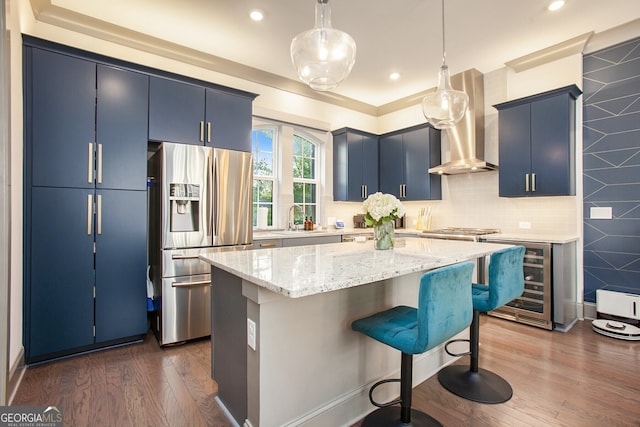 kitchen with beverage cooler, stainless steel appliances, a sink, wall chimney range hood, and blue cabinetry