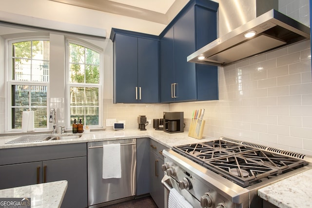 kitchen featuring blue cabinetry, stainless steel appliances, backsplash, a sink, and wall chimney exhaust hood