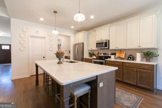 kitchen with dark wood finished floors, a breakfast bar area, appliances with stainless steel finishes, a sink, and an island with sink