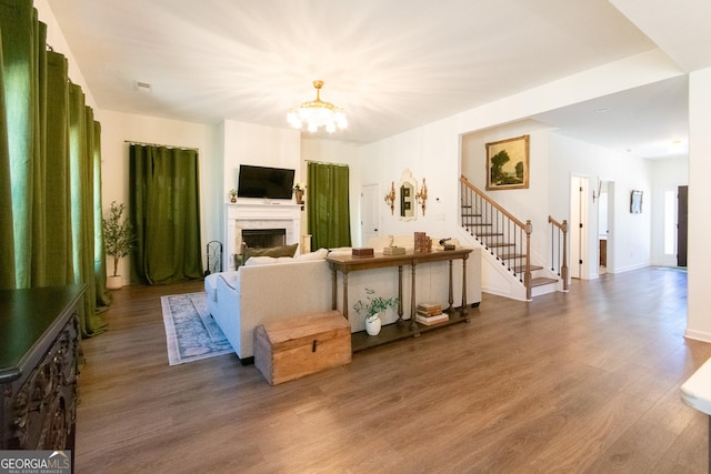 living area featuring baseboards, stairway, wood finished floors, a fireplace, and a chandelier