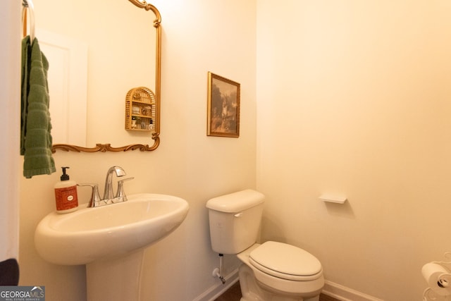 half bath featuring toilet, baseboards, and a sink