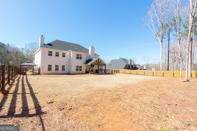 rear view of property featuring a gazebo, a chimney, a patio area, and a fenced backyard