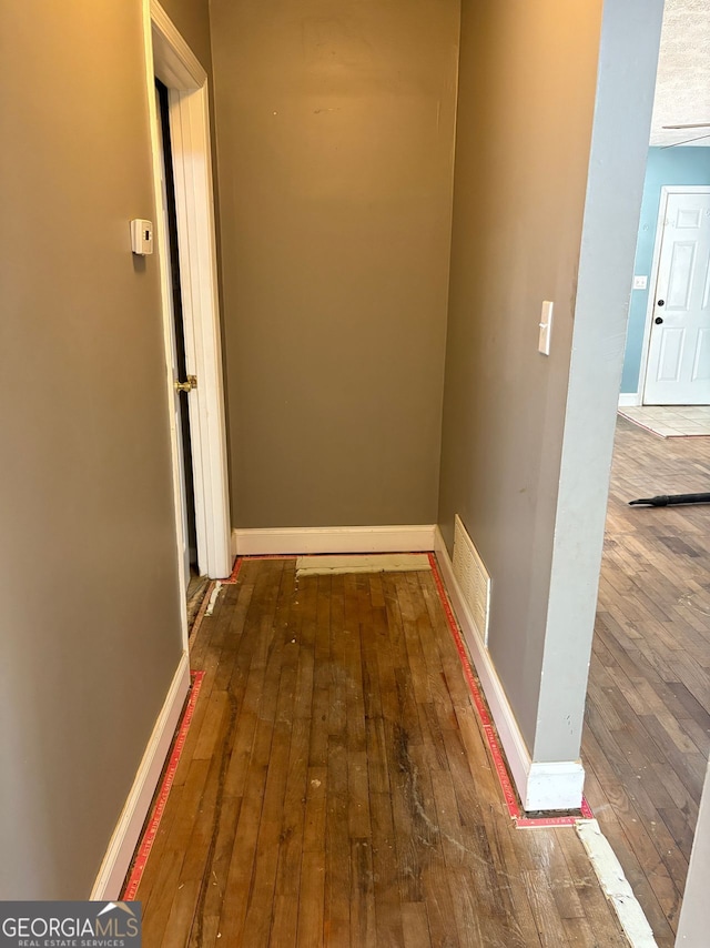 hall featuring hardwood / wood-style floors, visible vents, and baseboards