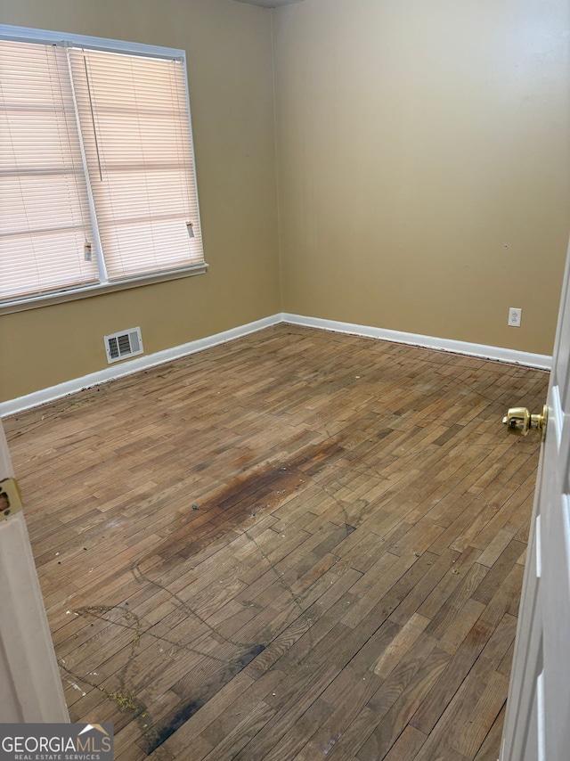 spare room with hardwood / wood-style flooring, baseboards, and visible vents