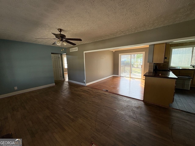 interior space featuring baseboards, visible vents, ceiling fan, dark wood-style flooring, and a textured ceiling