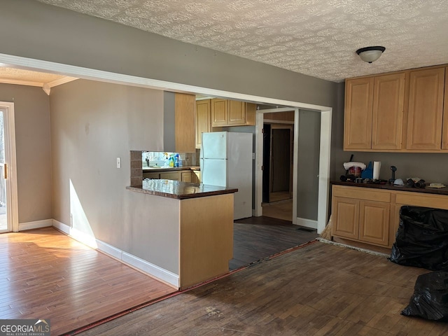 kitchen featuring a peninsula, baseboards, freestanding refrigerator, dark wood-style floors, and dark countertops