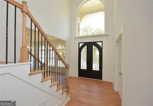 entrance foyer featuring stairs, a high ceiling, wood finished floors, and french doors