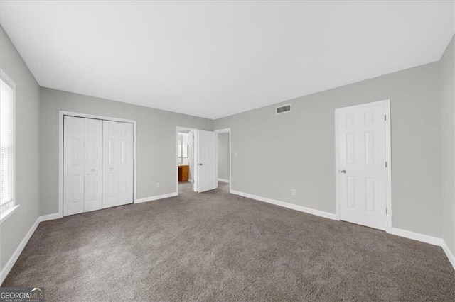 unfurnished bedroom with a closet, dark carpet, visible vents, and baseboards