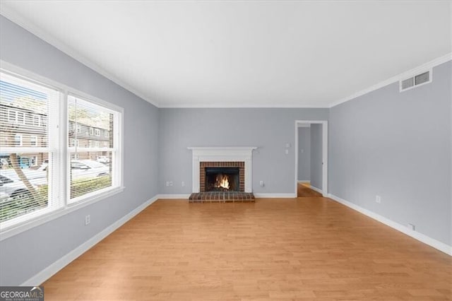 unfurnished living room with light wood-type flooring, a brick fireplace, baseboards, and ornamental molding