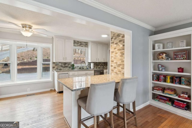 kitchen with crown molding, a sink, a kitchen breakfast bar, light stone countertops, and dishwashing machine