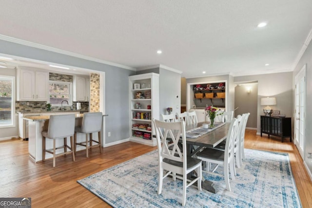 dining space with light wood-style floors, crown molding, and baseboards