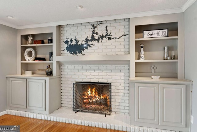 living room with ornamental molding, a brick fireplace, wood finished floors, and built in shelves