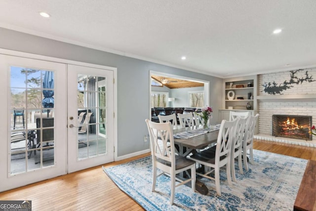 dining area with a textured ceiling, a fireplace, french doors, wood-type flooring, and crown molding