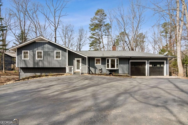 split level home featuring aphalt driveway, a chimney, an attached garage, and a shingled roof