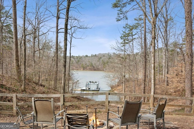 view of patio / terrace featuring a fire pit, a forest view, a water view, and fence