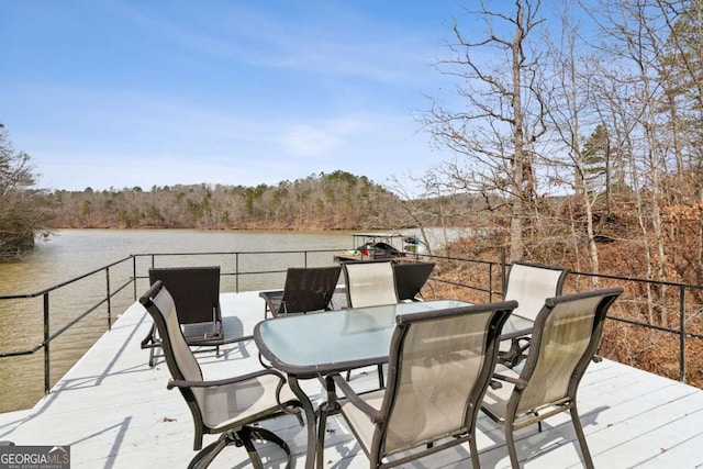 deck featuring outdoor dining space, a water view, and a wooded view