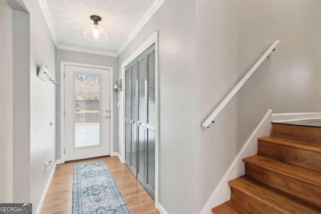 doorway with crown molding, baseboards, stairs, and light wood-style floors