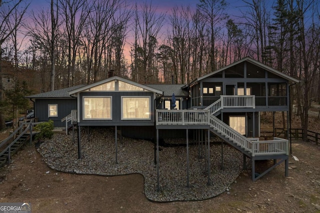 back of house at dusk with a sunroom, stairway, a deck, and roof with shingles