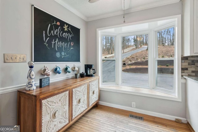 interior space with baseboards, crown molding, visible vents, and wood finished floors