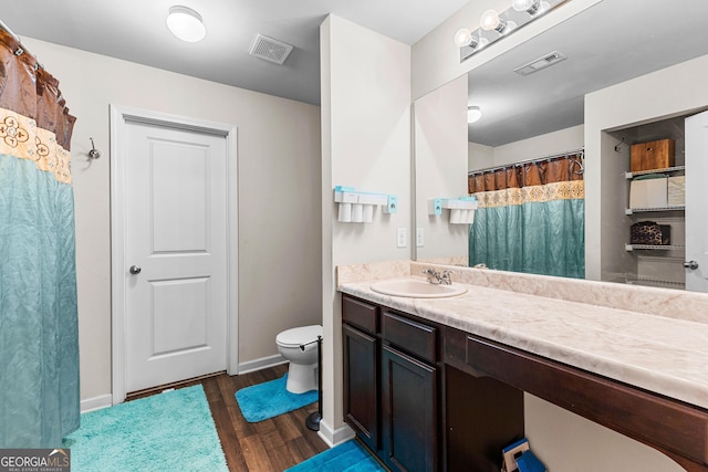 bathroom featuring visible vents, baseboards, toilet, wood finished floors, and vanity