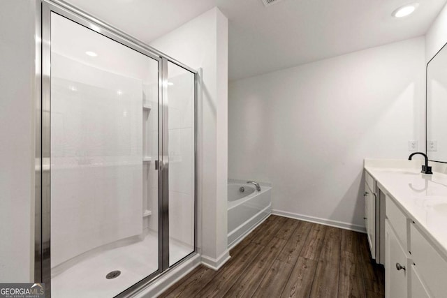 bathroom featuring wood finished floors, double vanity, a sink, a shower stall, and a garden tub