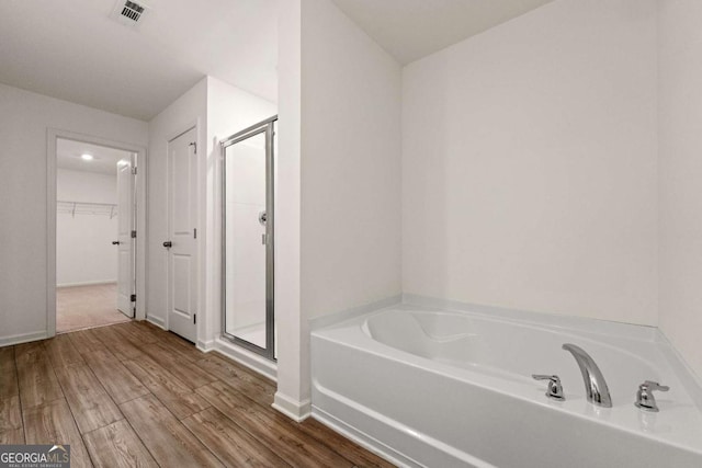 bathroom with a stall shower, wood finished floors, a spacious closet, and a bath