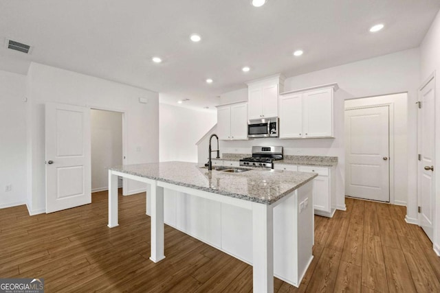 kitchen with wood finished floors, a center island with sink, a sink, white cabinets, and appliances with stainless steel finishes